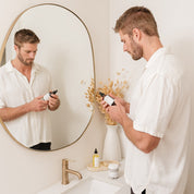 Man using Room & Linen Spray product in front of a mirror in a bathroom.