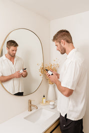 Man using Room & Linen Spray product in front of a mirror in a bathroom.