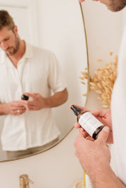 Man holding a bottle of Room & Linen Spray in front of a mirror