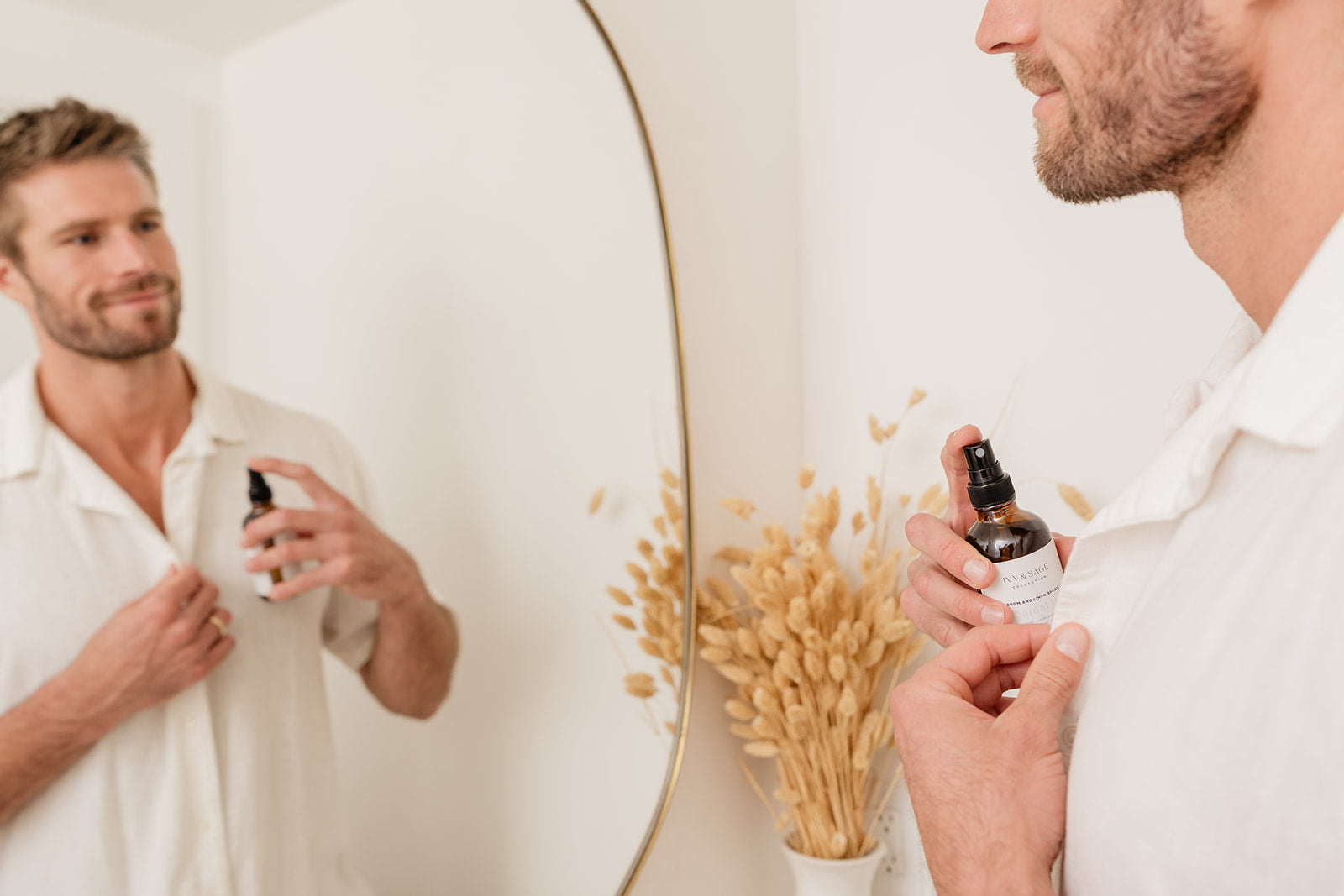Man holding a bottle of Room & Linen Spray in front of a mirror with a neutral background