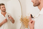 Man holding a bottle of Room & Linen Spray in front of a mirror with a neutral background