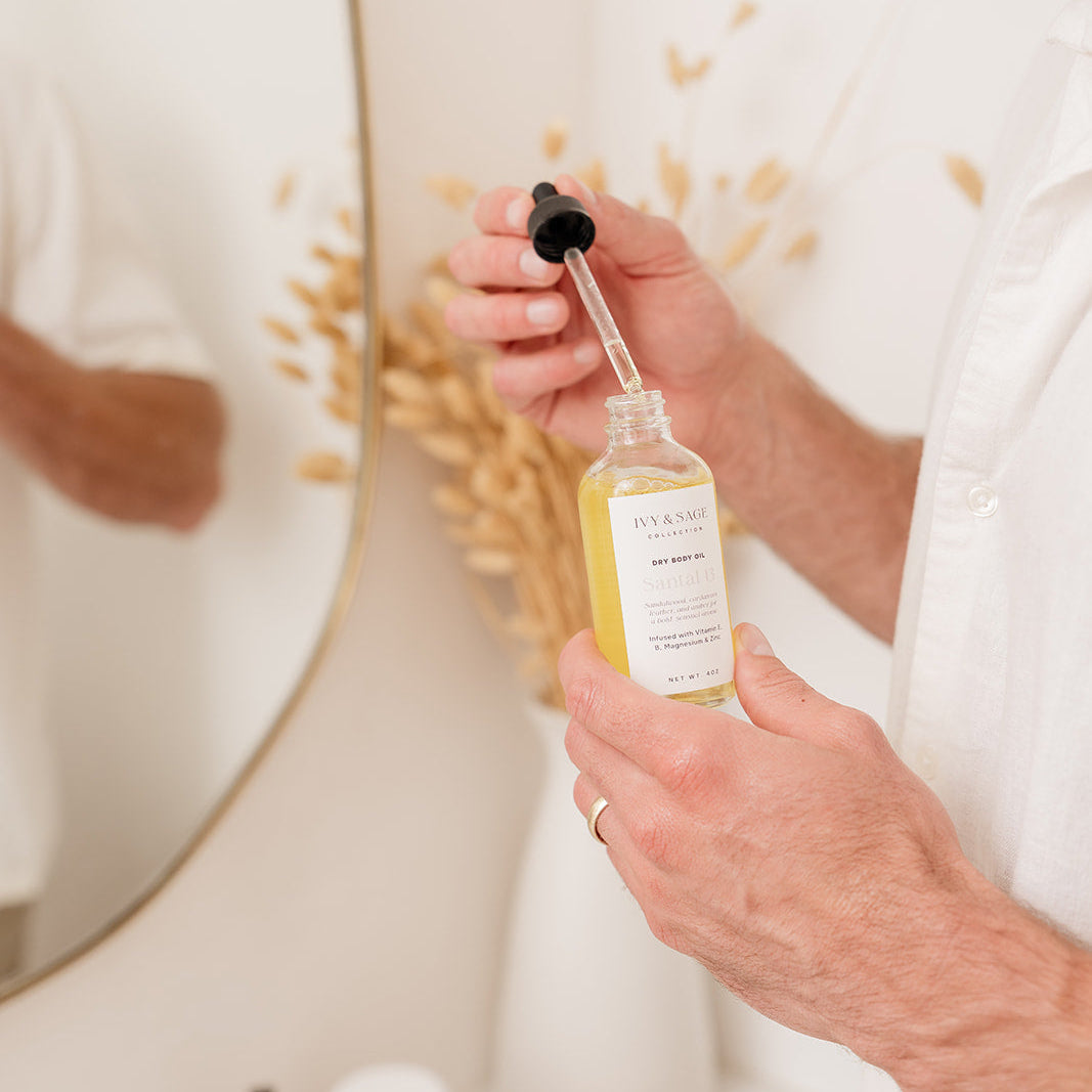 Man holding a bottle of body oil with dropper in a bathroom setting