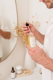 Man holding a bottle of body oil with dropper in a bathroom setting
