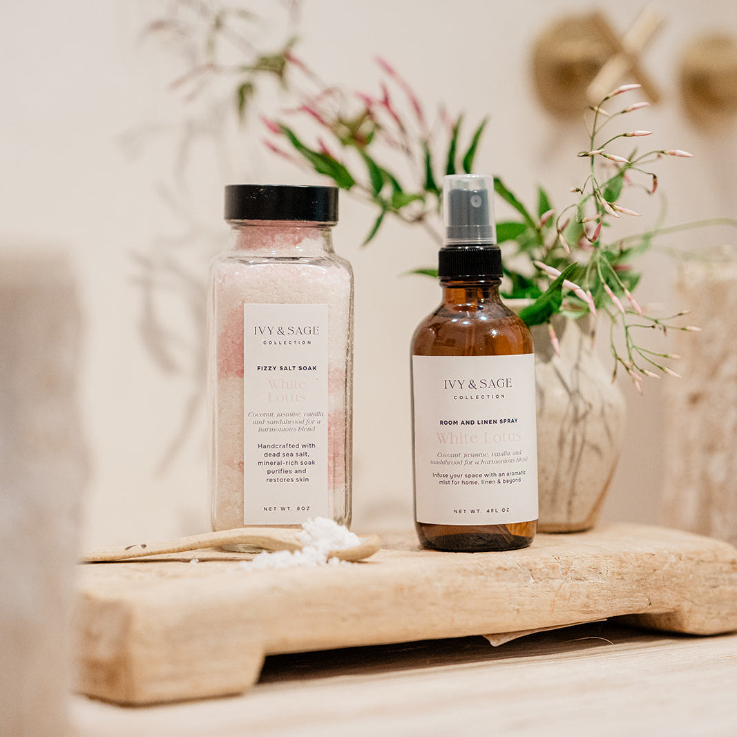 Two bottles of Ivy & Sage products on a wooden surface next to sinks in bathroom with a blurred background
