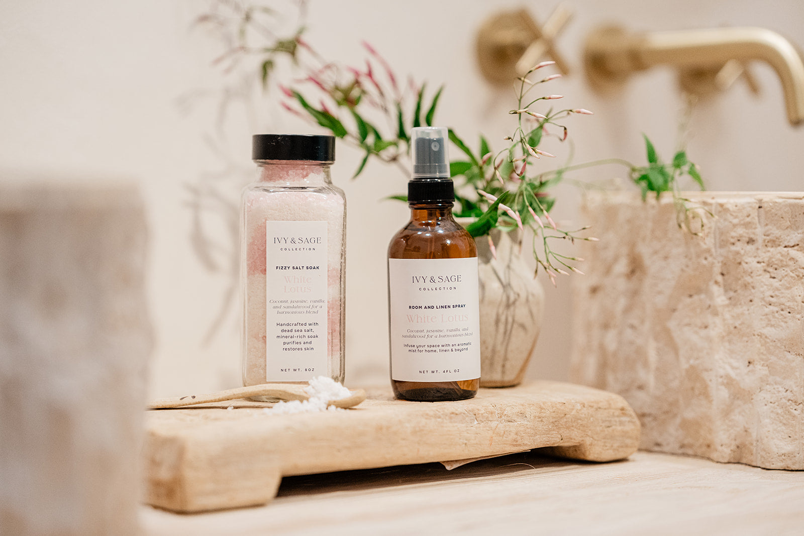 Two bottles of Ivy & Sage products on a wooden surface next to sinks in bathroom with a blurred background