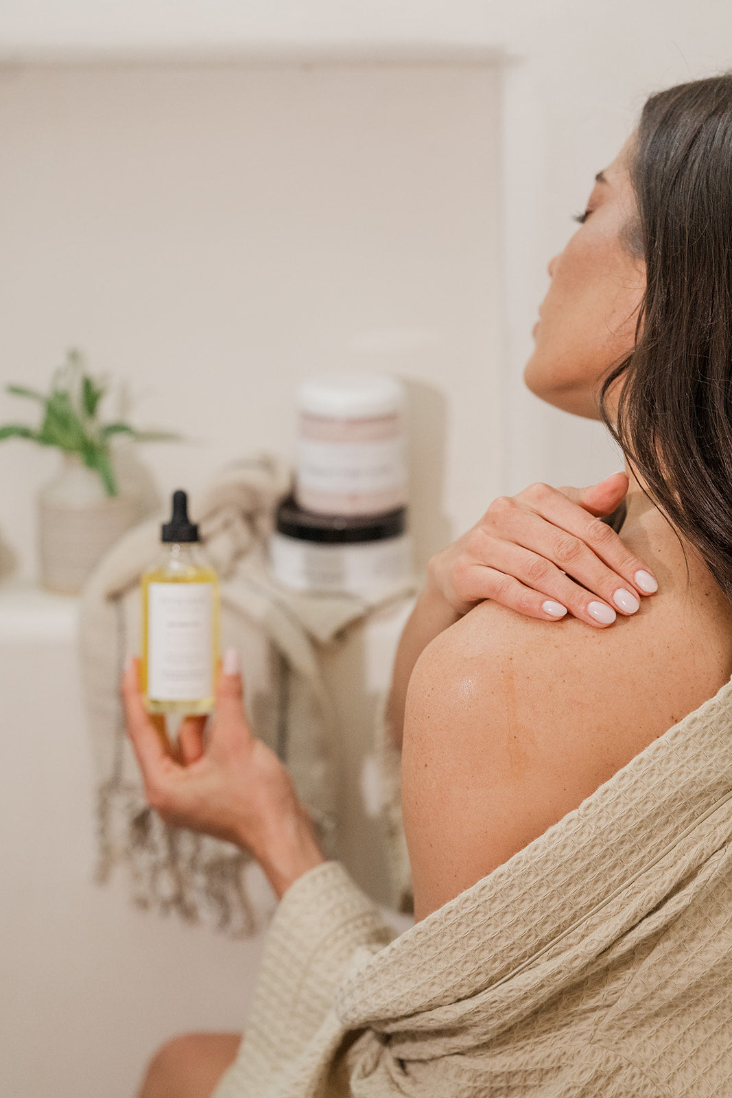 Woman applying a body oil to her shoulder in a bathroom in a cozy evening setting