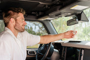 Man inside a vehicle holding a glass car diffuser bottle handing on rear view mirror