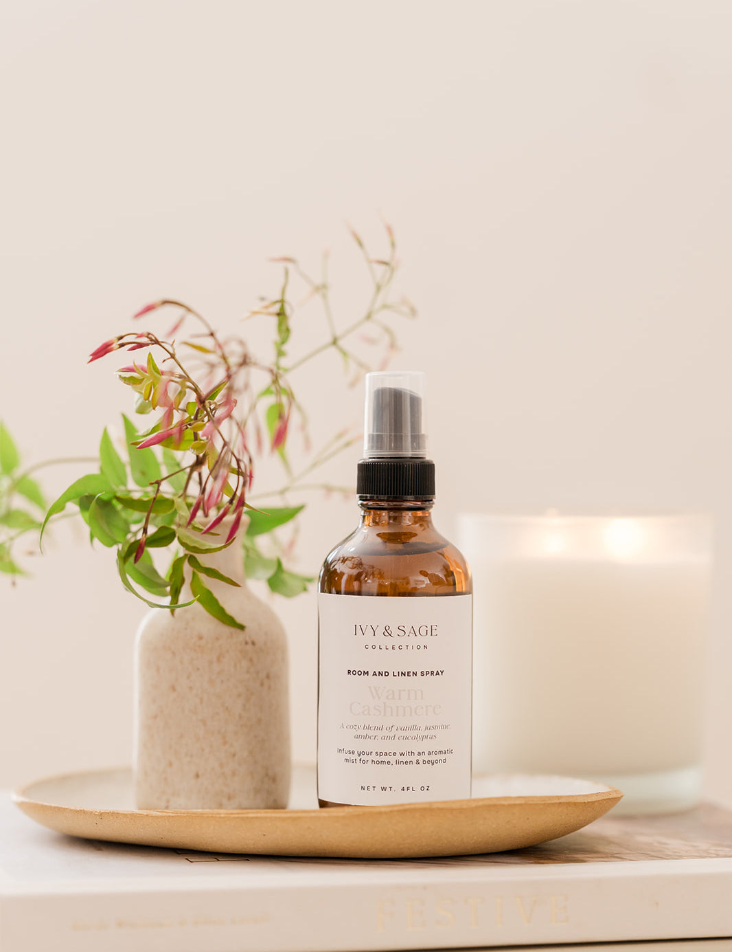 Bottle on Room & Linen Spray on a tray sitting in a bowl on a book with a vase and lit candle