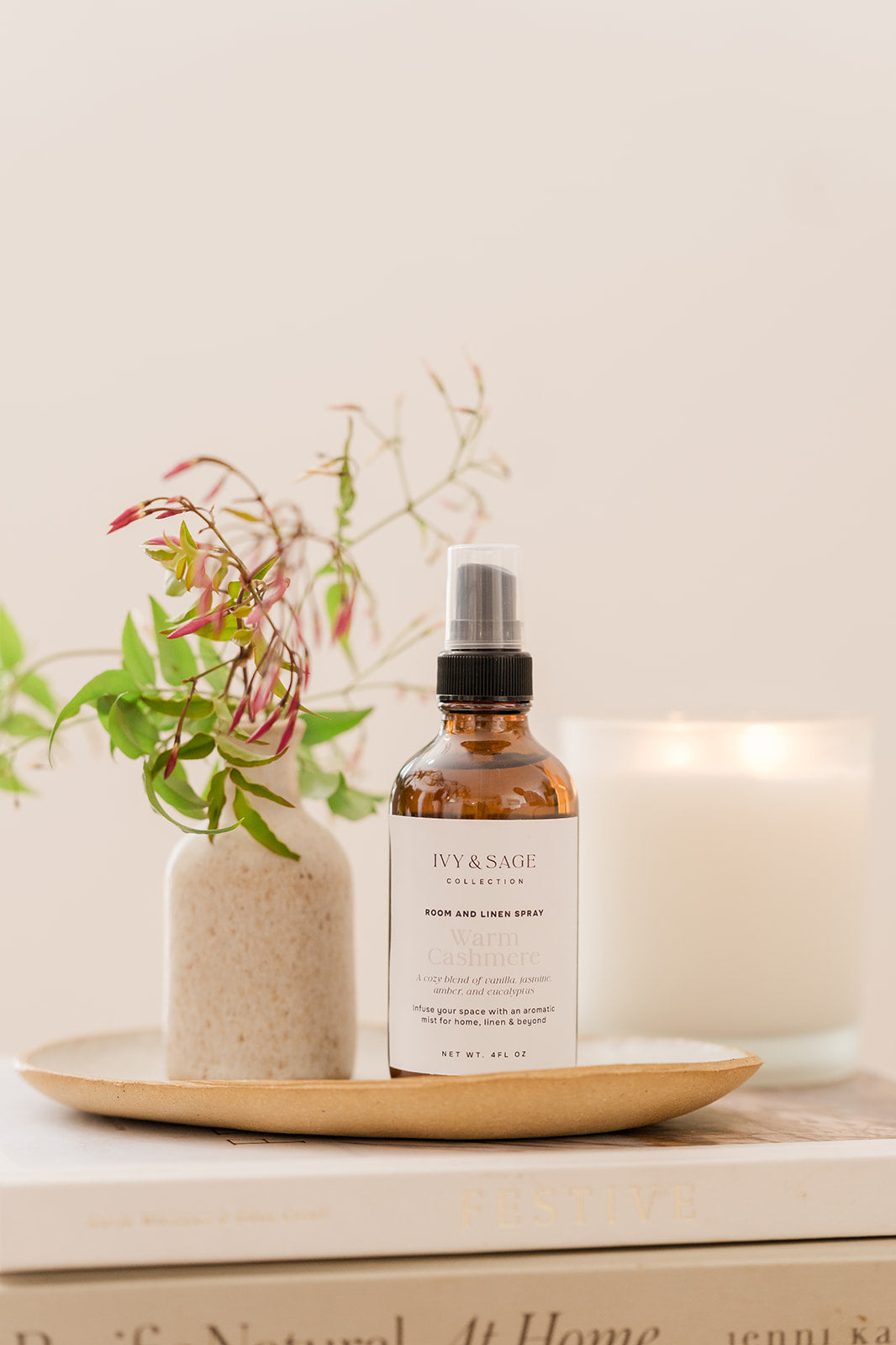 Bottle on Room & Linen Spray on a tray sitting in a bowl on a book with a vase and lit candle