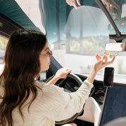 Woman sitting inside a vehicle, holding a glass car diffuser 