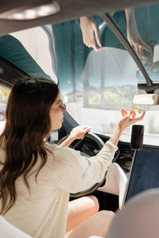 Woman sitting inside a vehicle, holding a glass car diffuser 