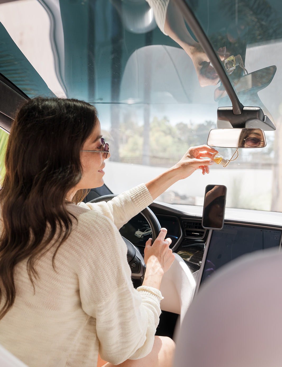 Woman sitting inside a car, holding a glass car diffuser hung on rear view mirror