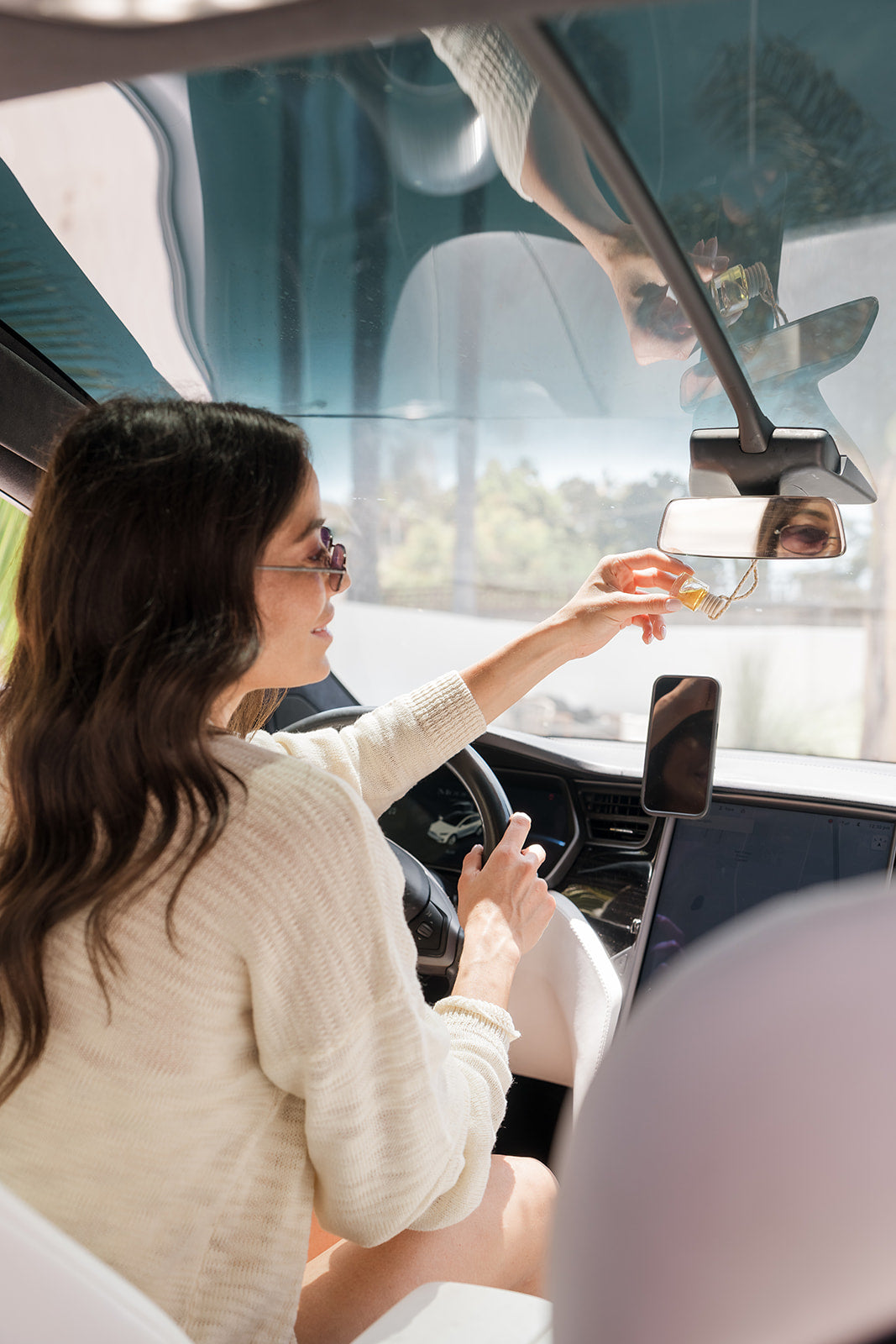 Woman sitting inside a car, holding a glass car diffuser hung on rear view mirror