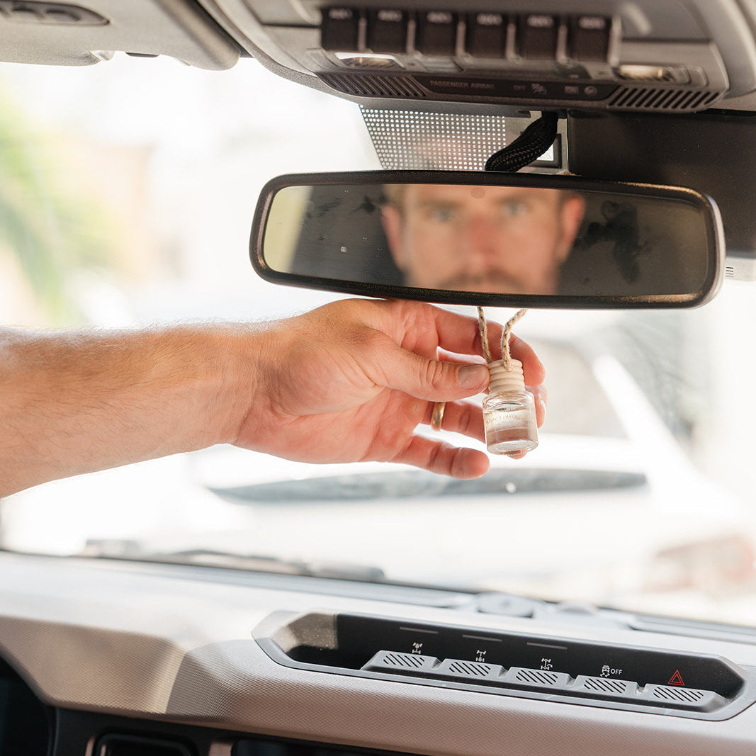 Hand holding a glass car diffuser hanging on a rear view mirror with a blurred background