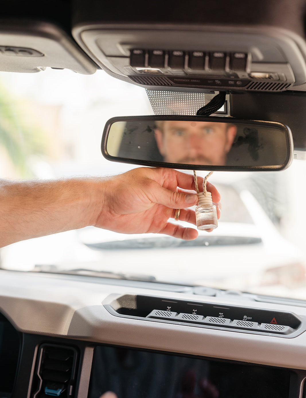 Hand holding a glass car diffuser hanging on a rear view mirror with a blurred background