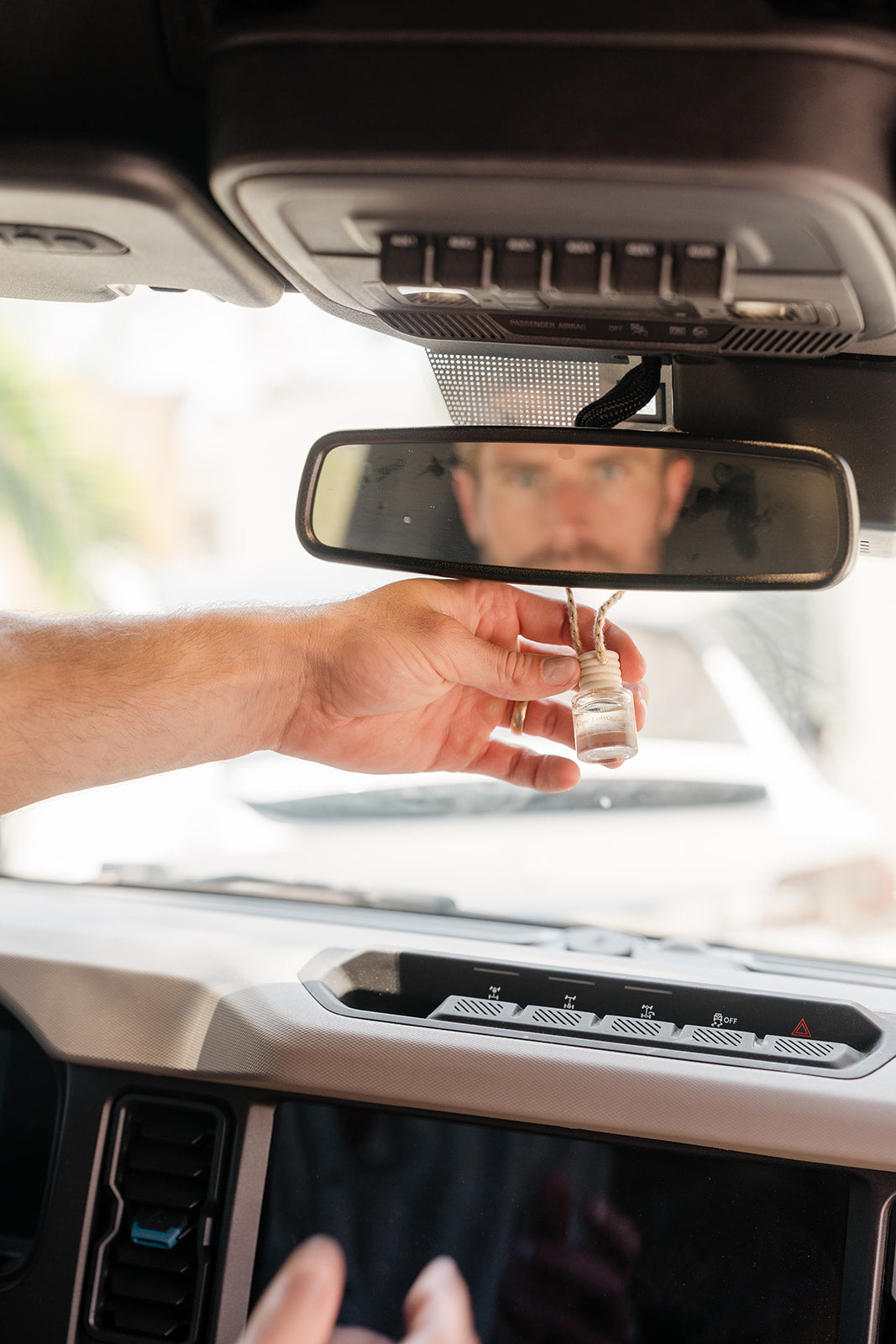 Hand holding a glass car diffuser hanging on a rear view mirror with a blurred background