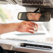 Hand holding a glass car diffuser hanging on a rear view mirror with a blurred background