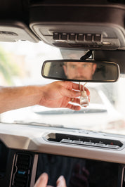 Hand holding a glass car diffuser hanging on a rear view mirror with a blurred background