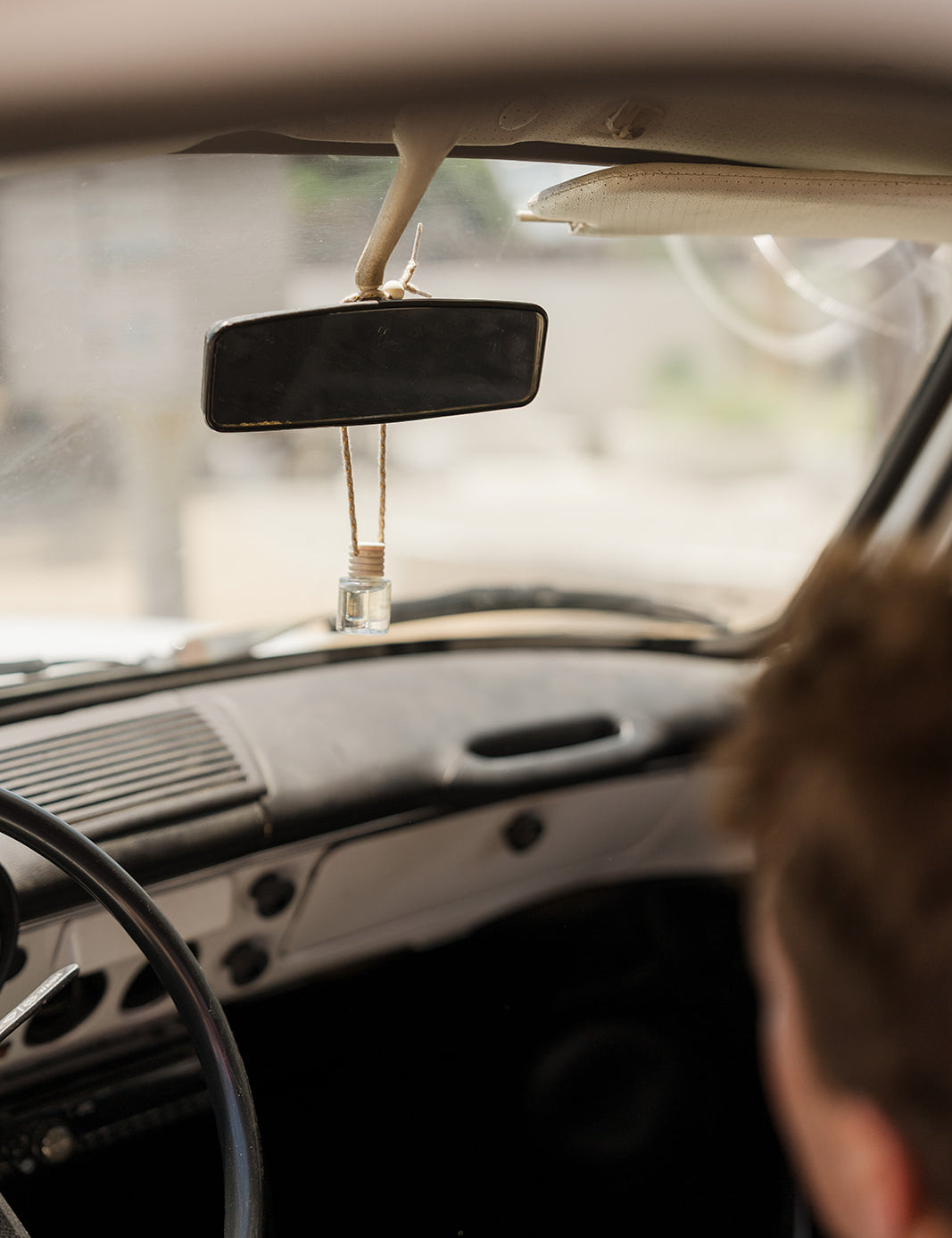 Person sitting inside a car looking out the windshield with a rearview mirror car diffuser