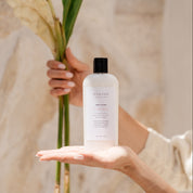Person holding a bottle of Body Lotion skincare product with a leaf in the background
