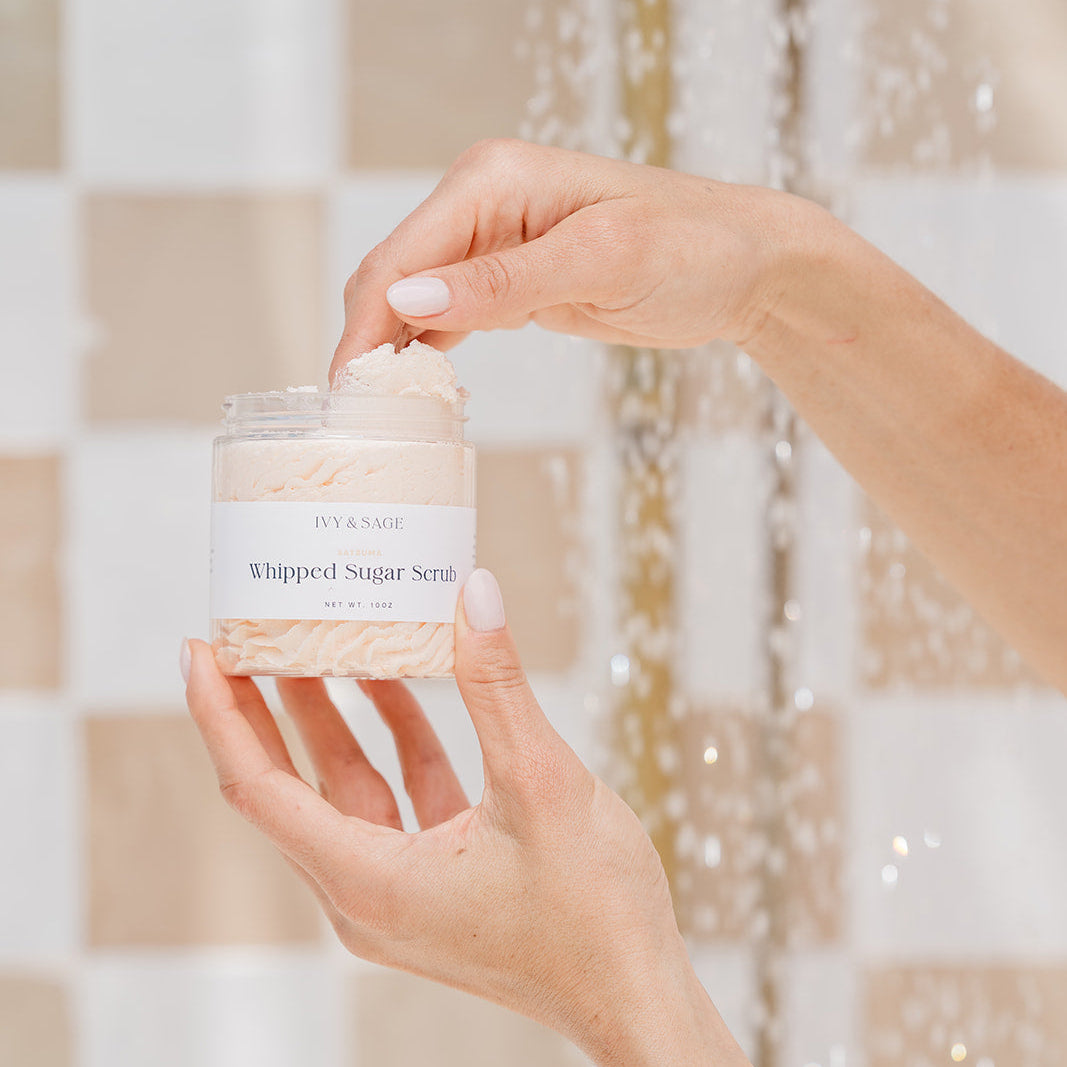 Hand holding a jar of whipped sugar scrub in a shower
