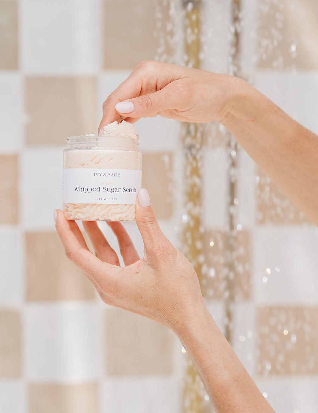 Hand holding a jar of whipped sugar scrub in a shower