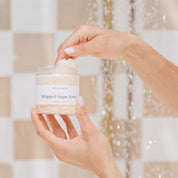 Hand holding a jar of whipped sugar scrub in a shower