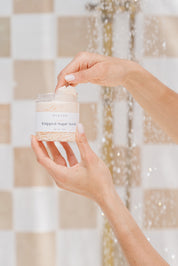 Hand holding a jar of whipped sugar scrub in a shower