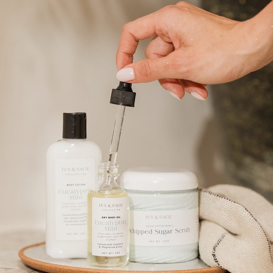 Hand holding a dropper over a bottle of skincare product on a wooden tray with other skincare items.