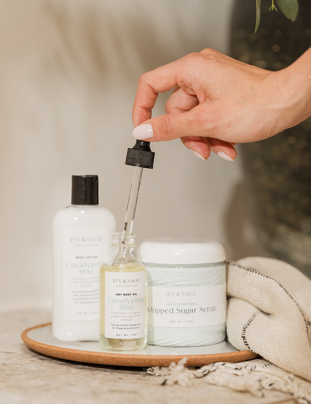 Hand holding a dropper over a bottle of skincare product on a wooden tray with other skincare items.
