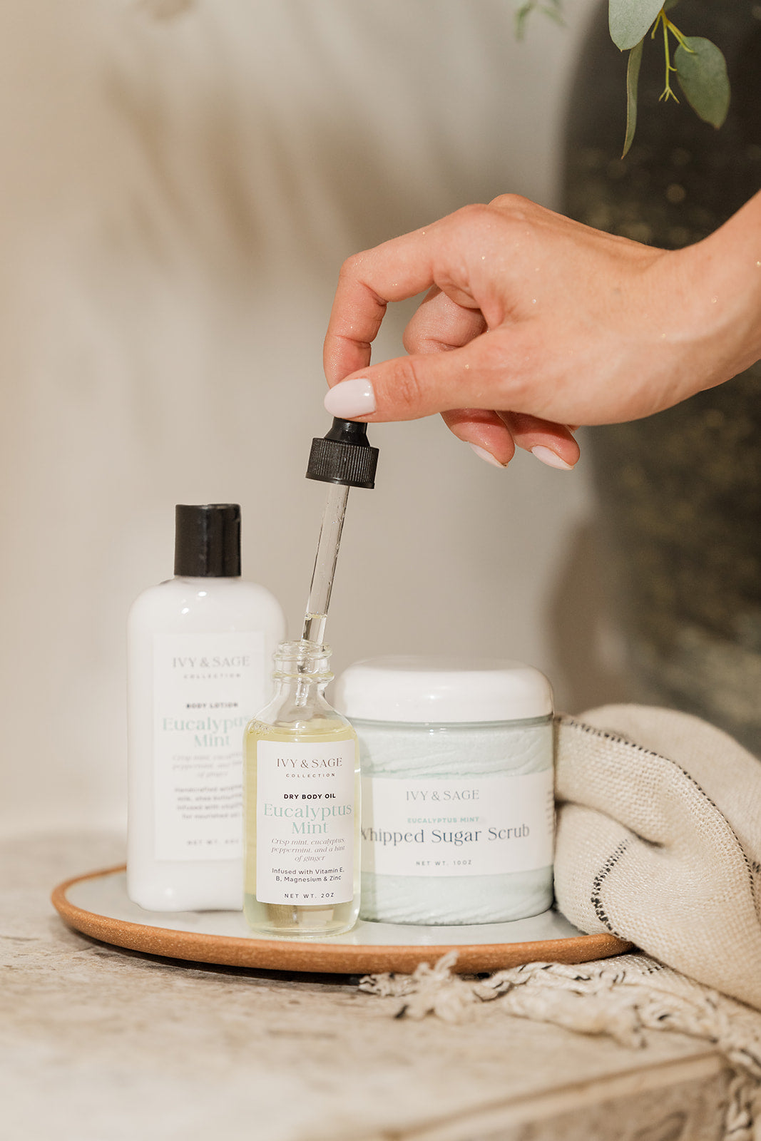 Hand holding a dropper over a bottle of skincare product on a wooden tray with other skincare items.