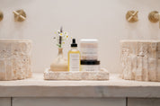 Bathroom counter with skincare products and decorative items on a neutral background. Including oil, sugar scrub and body butter