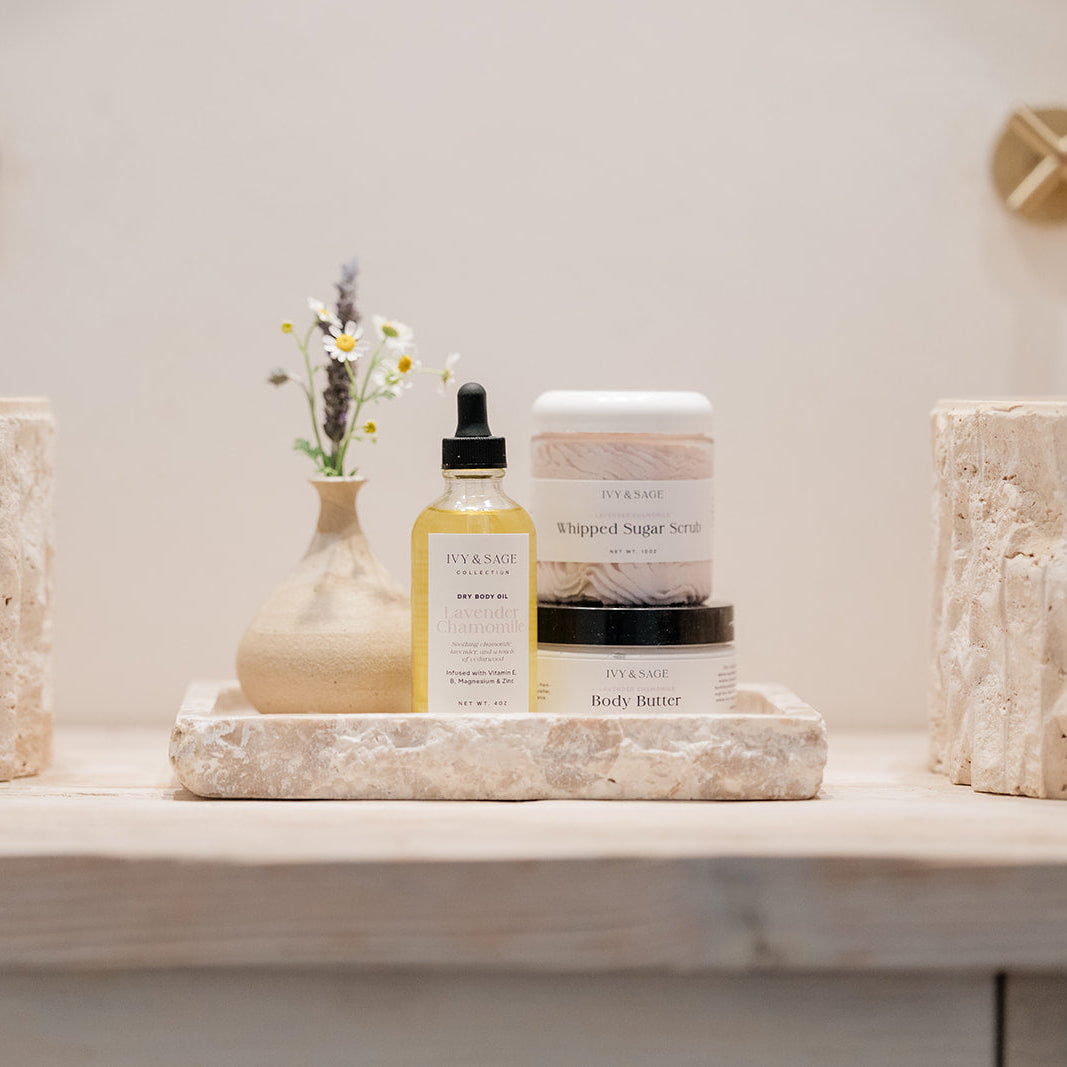 Bathroom counter with skincare products and decorative items on a neutral background. Including oil, sugar scrub and body butter