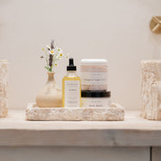 Bathroom counter with skincare products and decorative items on a neutral background. Including oil, sugar scrub and body butter