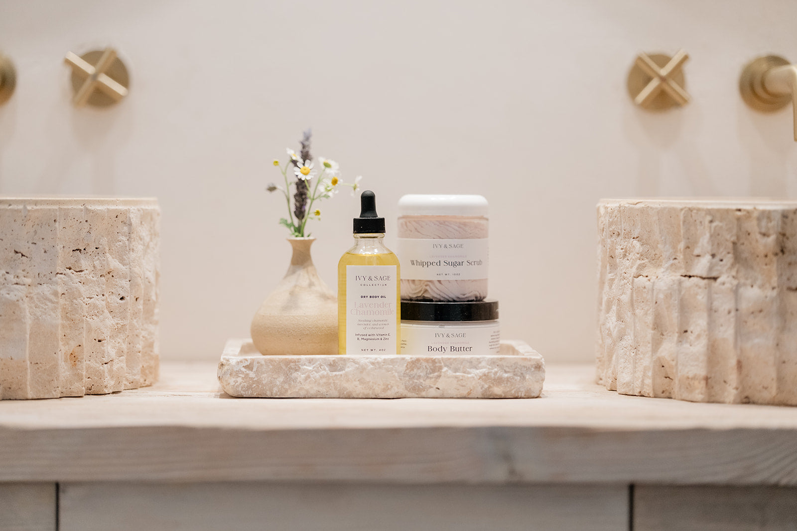 Bathroom counter with skincare products and decorative items on a neutral background. Including oil, sugar scrub and body butter