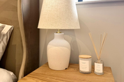 Ivy & Sage reed diffuser styled on a bedside table in a warm, neutral home interior alongside coordinating home fragrance products.