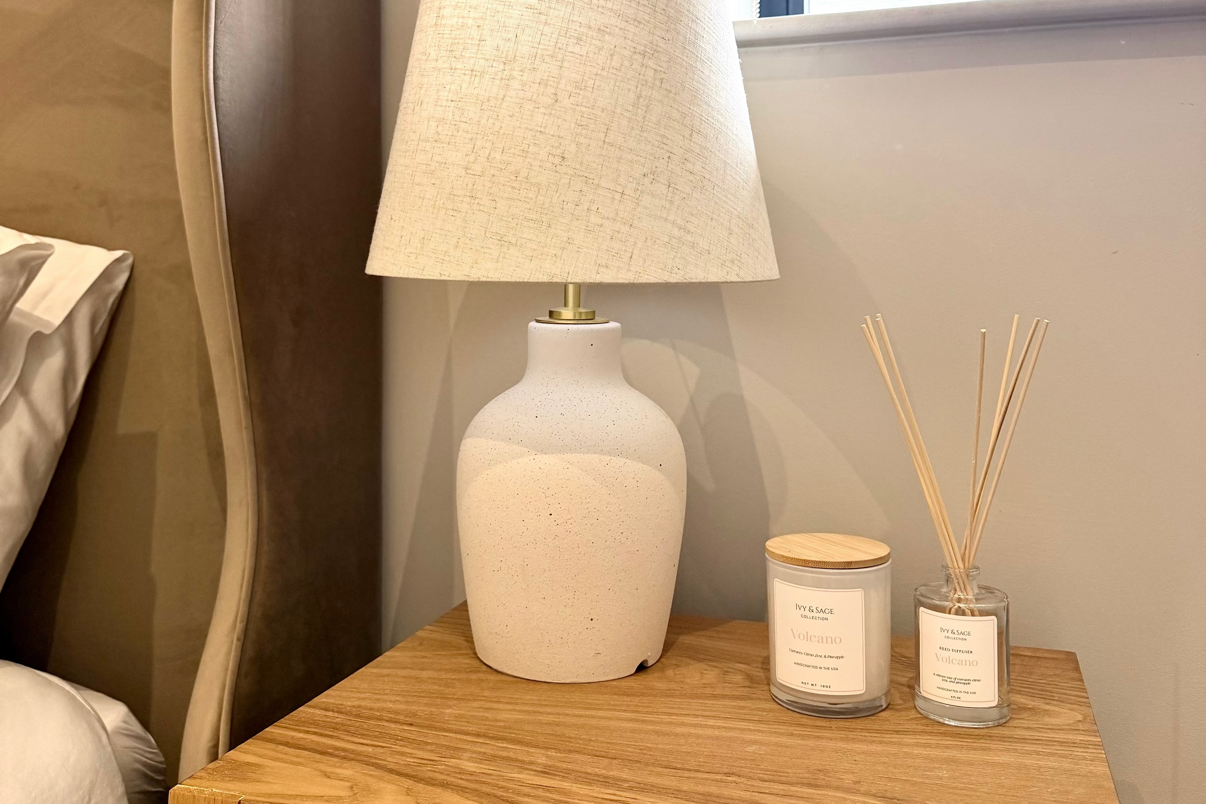 Ivy &amp; Sage reed diffuser styled on a bedside table in a warm, neutral home interior alongside coordinating home fragrance products.