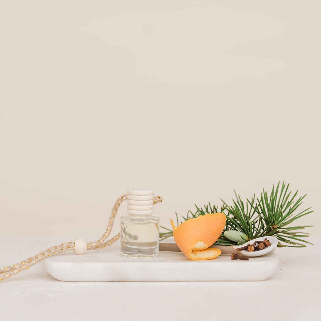 Car Diffuser glass jar with orange peel, and pine branch on a white marble slab against a beige background in Christmas Morning Scent