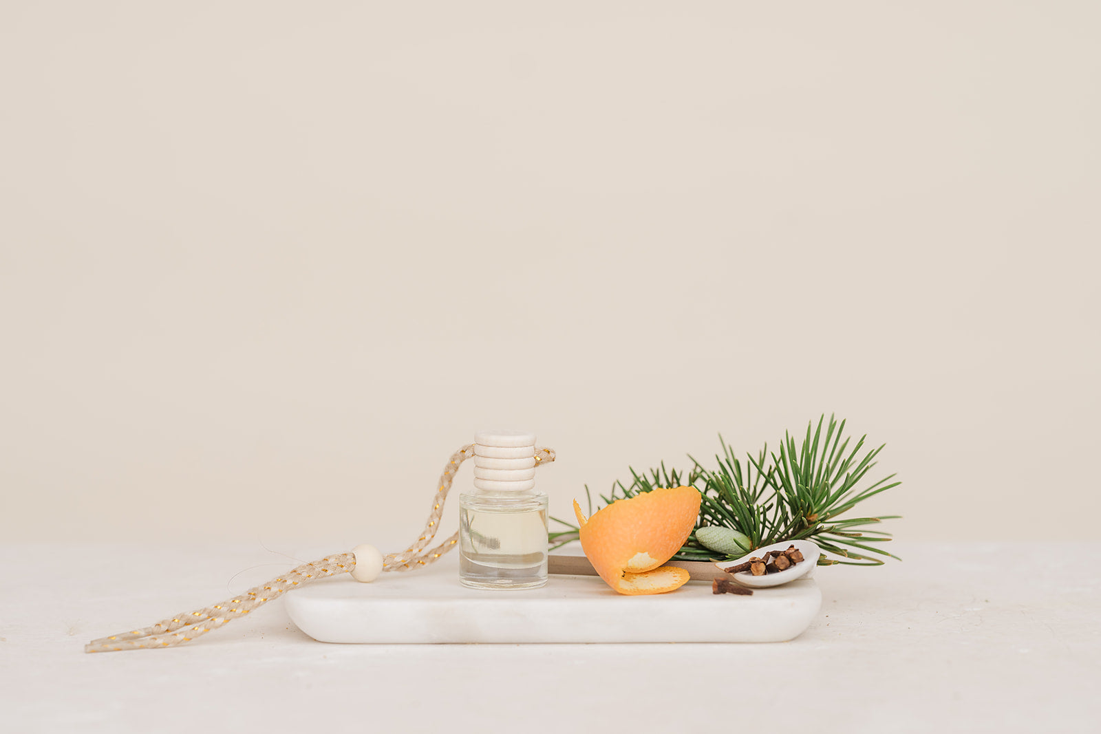 Car Diffuser glass jar with orange peel, and pine branch on a white marble slab against a beige background in Christmas Morning Scent