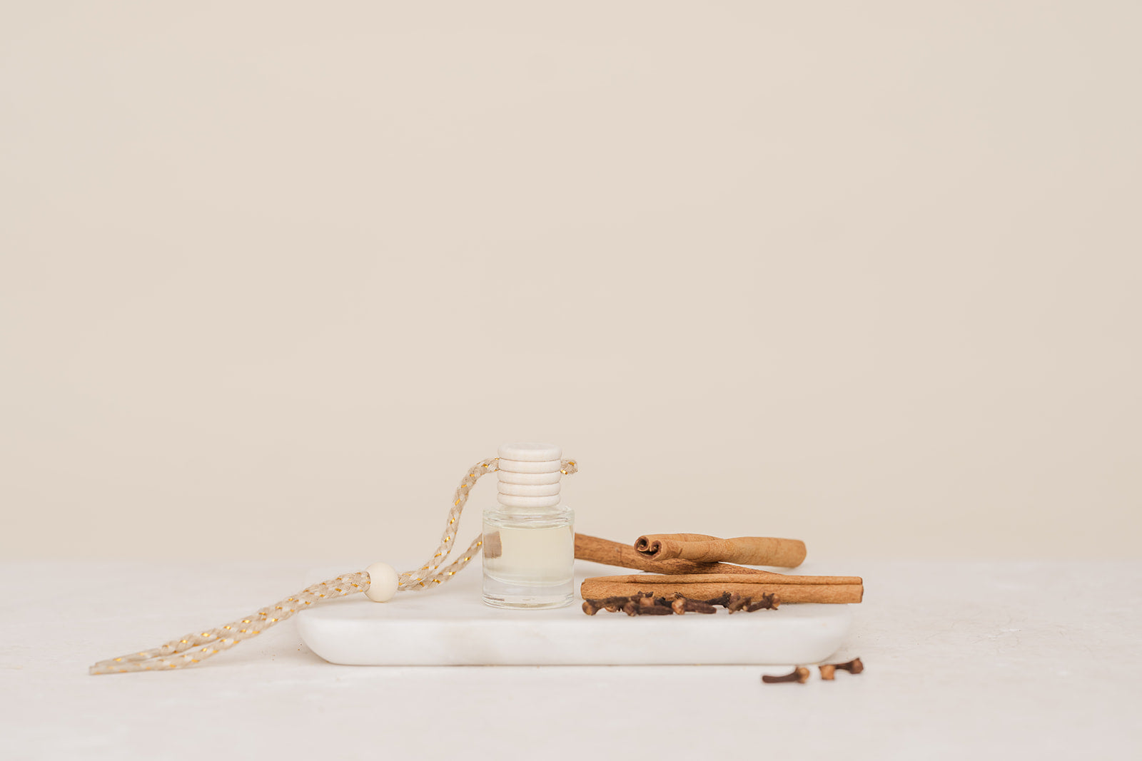 Glass Car Diffuser bottle with cinnamon sticks on a marble slab with light beige background
