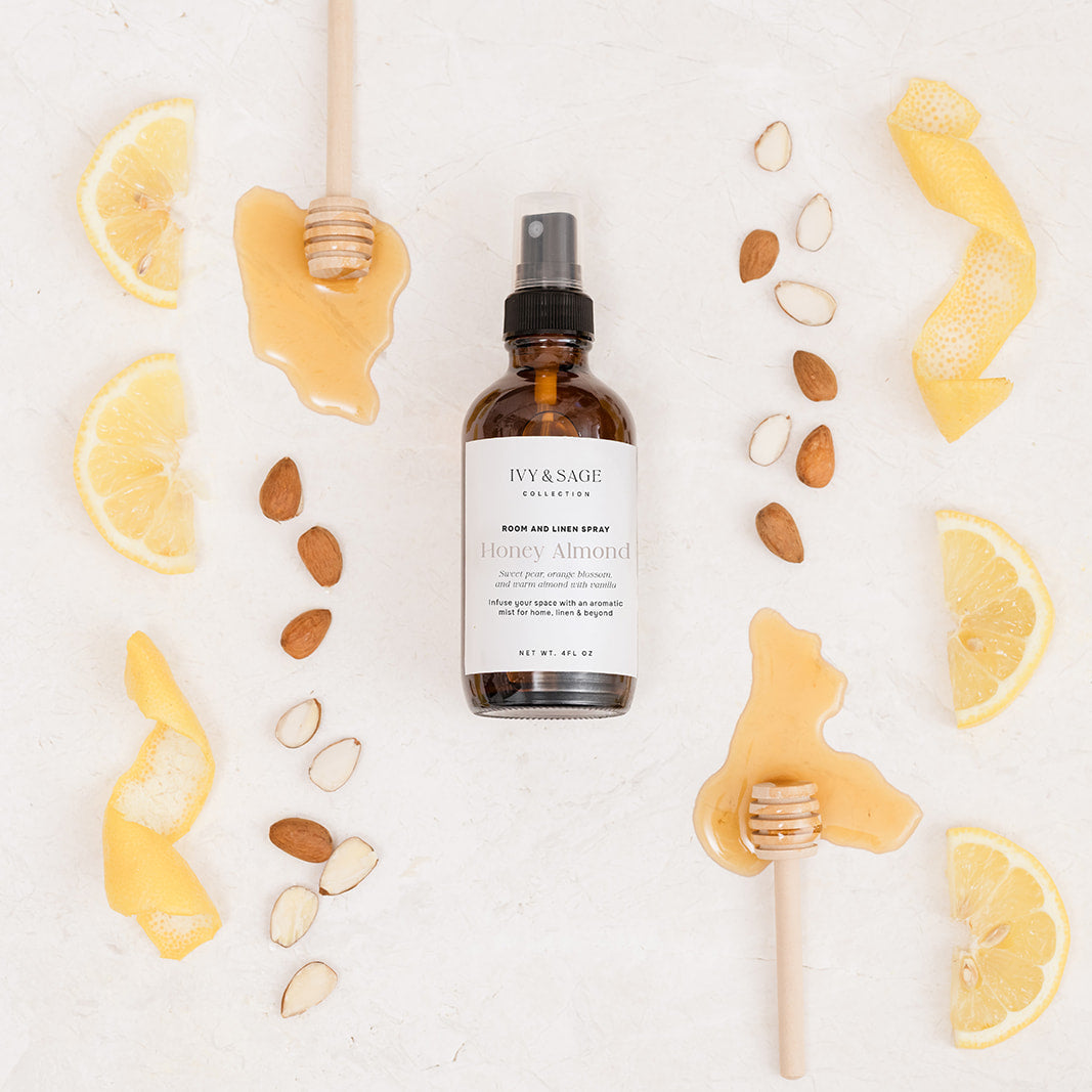 Bottle of Room & Linen Spray surrounded by lemons, honey and almonds on a white background