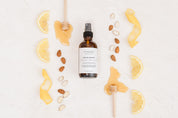 Bottle of Room & Linen Spray surrounded by lemons, honey and almonds on a white background