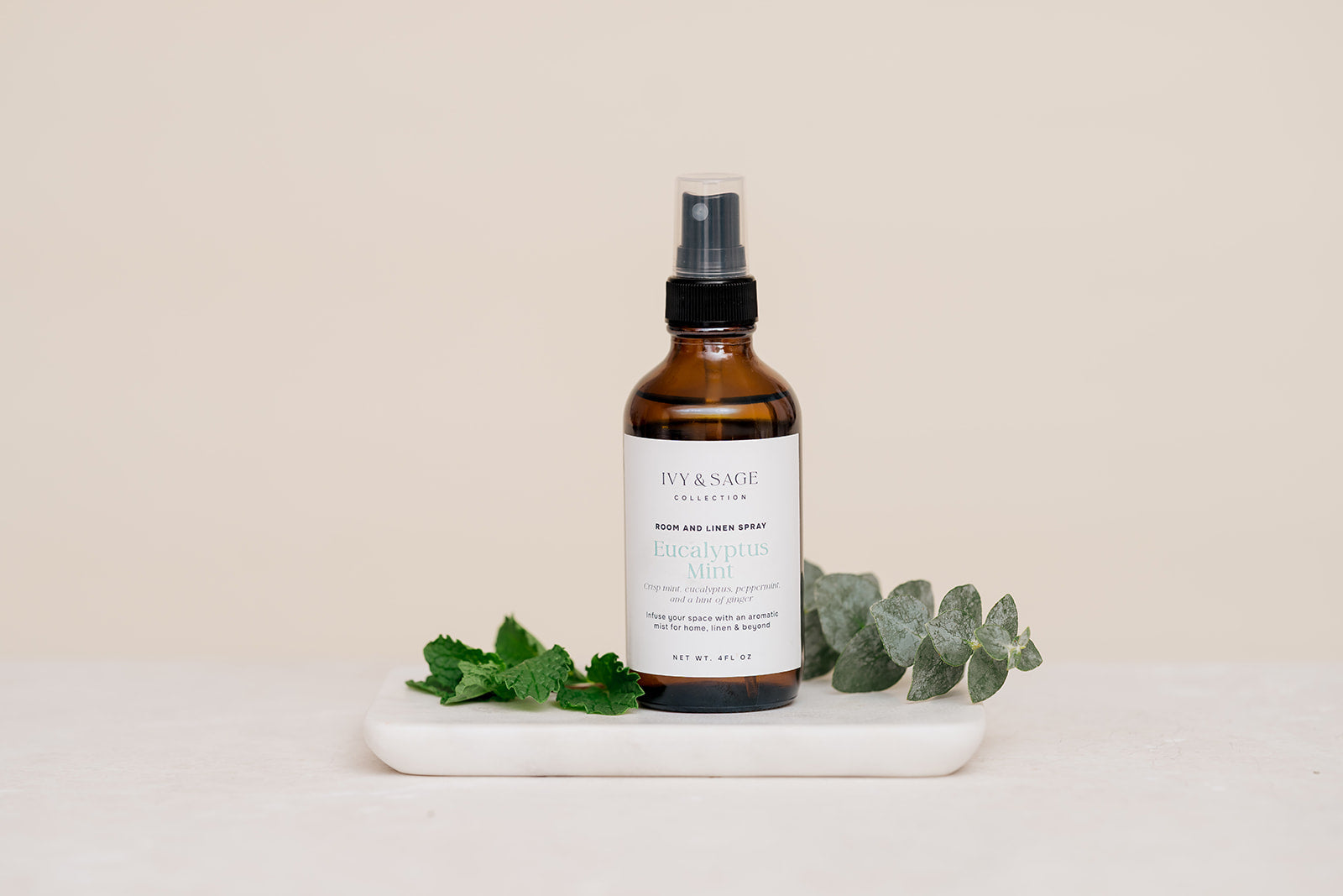 Bottle of Room & Linen Spray on a white tray with green leaves on a beige background