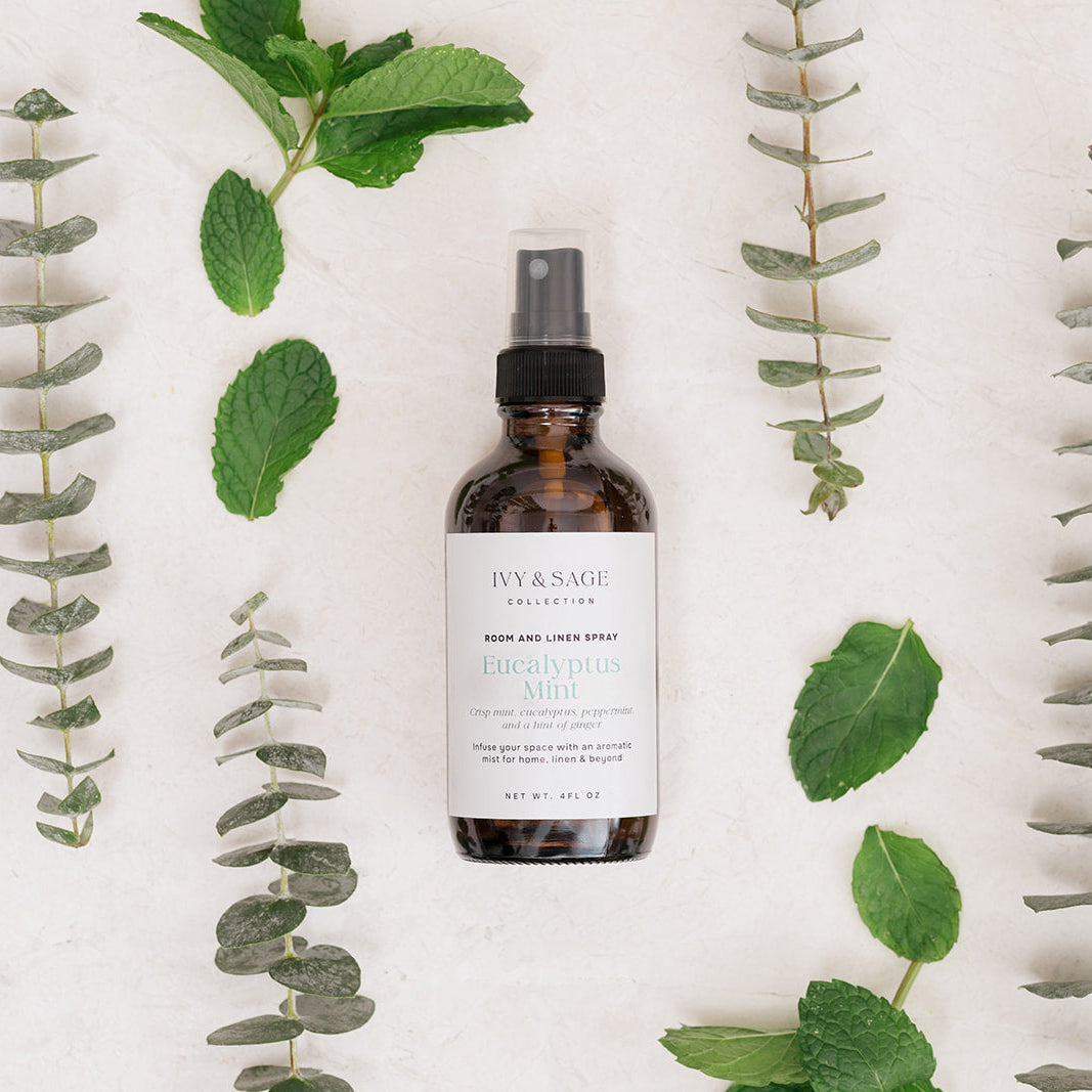 Bottle of Room & Linen Spray surrounded by eucalyptus leaves on a white background