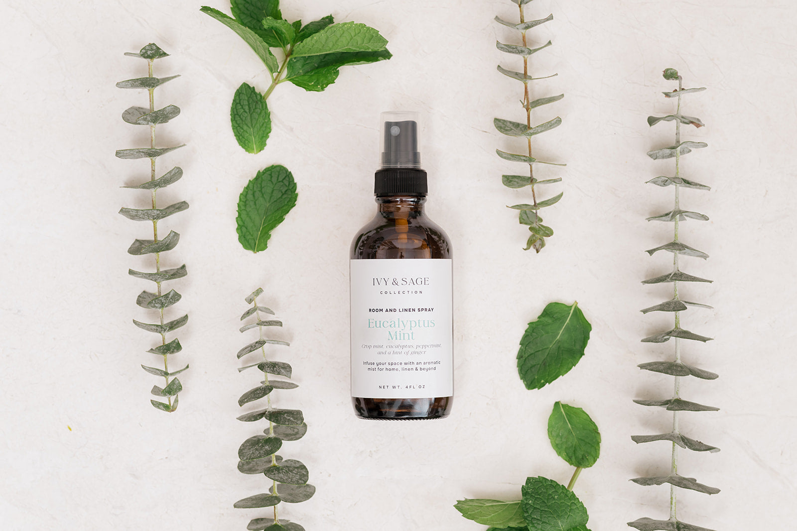 Bottle of Room & Linen Spray surrounded by eucalyptus leaves on a white background