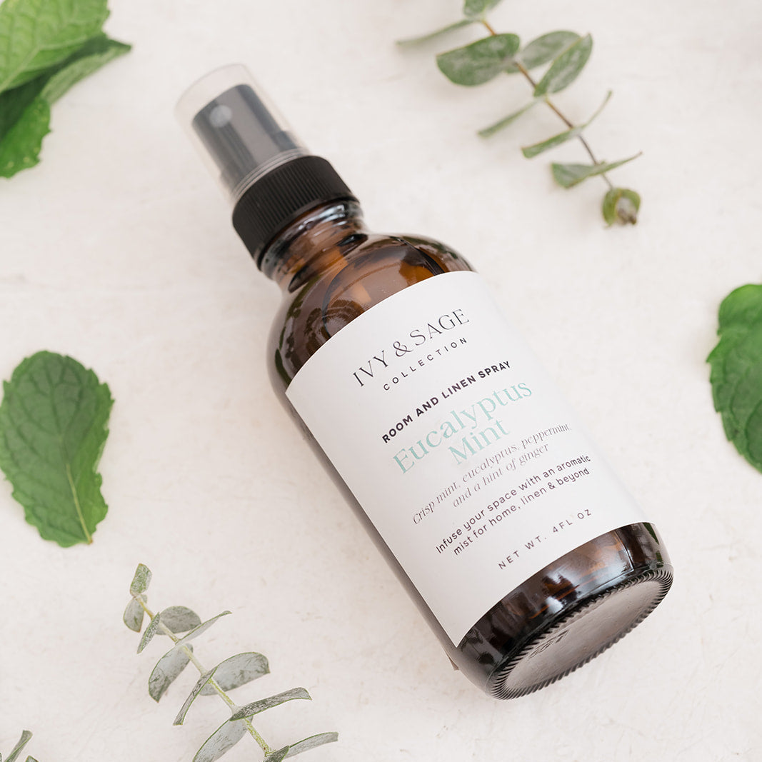 Bottle of Ivy & Sage Room & Linen Spray on a light background with Eucalyptus leaves