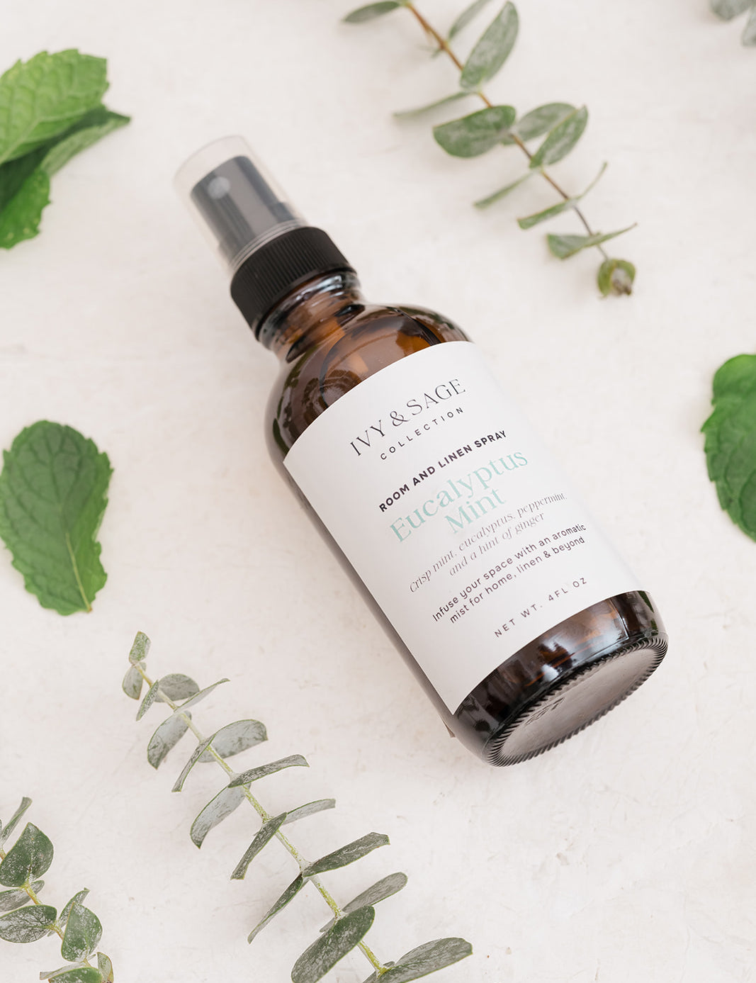 Bottle of Ivy & Sage Room & Linen Spray on a light background with Eucalyptus leaves