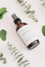 Bottle of Ivy & Sage Room & Linen Spray on a light background with Eucalyptus leaves