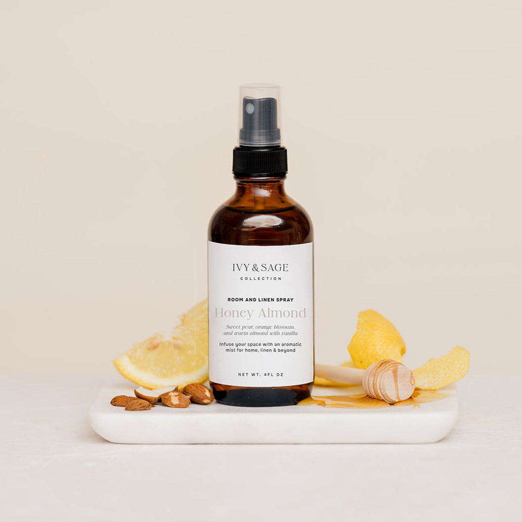 Bottle of Honey Almond body Room & Linen spray on a white surface with lemons, almonds and honey
