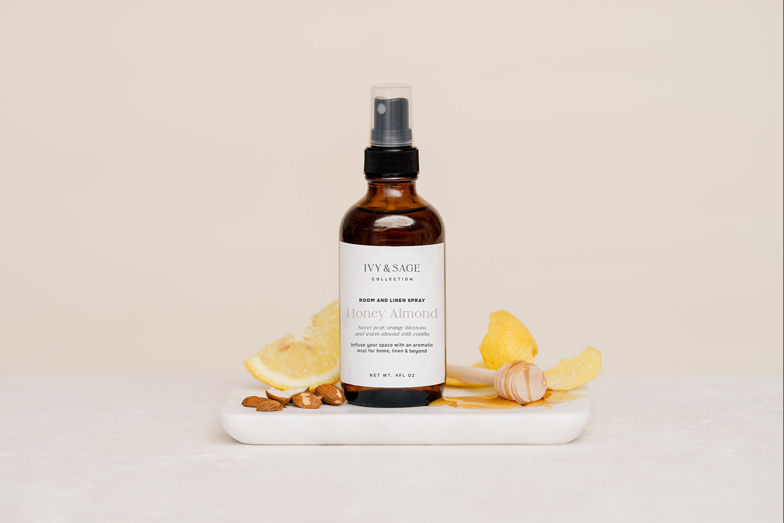 Bottle of Honey Almond body Room & Linen spray on a white surface with lemons, almonds and honey
